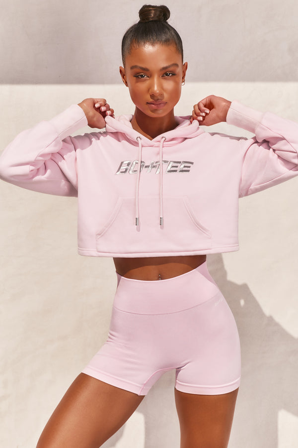 Pink long sleeved cropped hoodie with embroidered Bo+Tee logo across the chest. Image 1 of 6