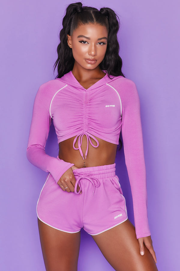 Purple long sleeve cropped hoodie with ruched centre and drawstring tie. Image 1 of 6.