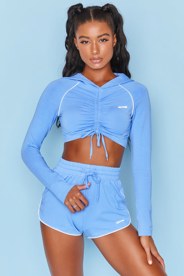 Bright blue long sleeve cropped hoodie with ruched centre and drawstring tie. Image 1 of 6.