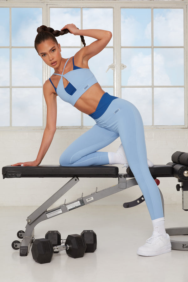 model leaning on gym bench in two toned blue womens gym leggings set