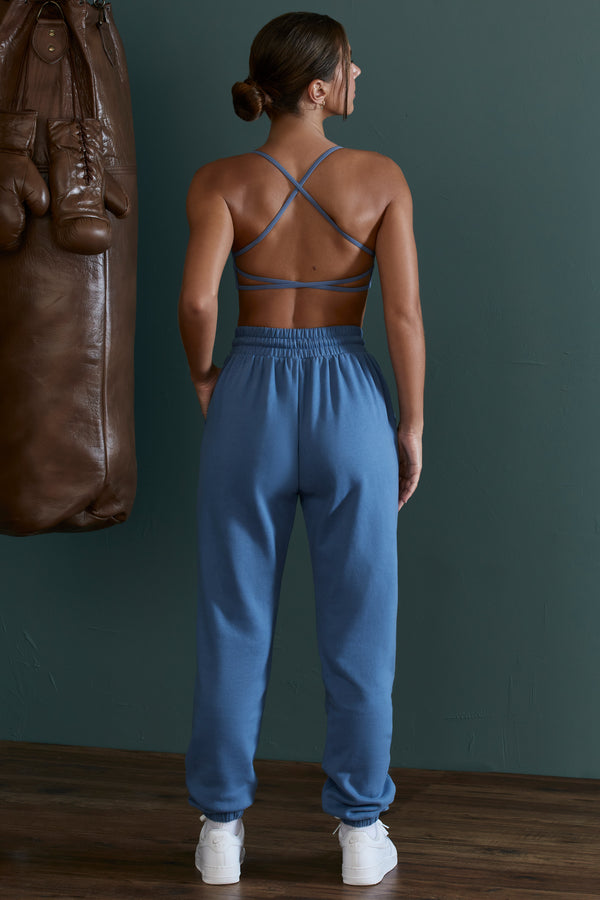 model showing back of crossed strap sports bra and matching blue jogger bottoms