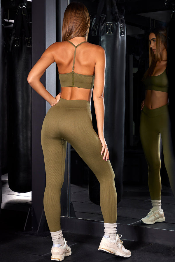 model posing to show back of petite high waisted ribbed leggings and sports bra in olive